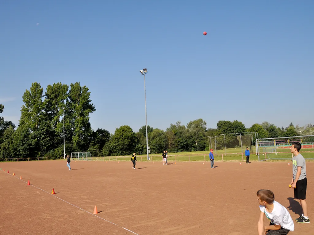 Jugendliche werfen auf dem Rasenplatz, der Ball fliegt hoch.